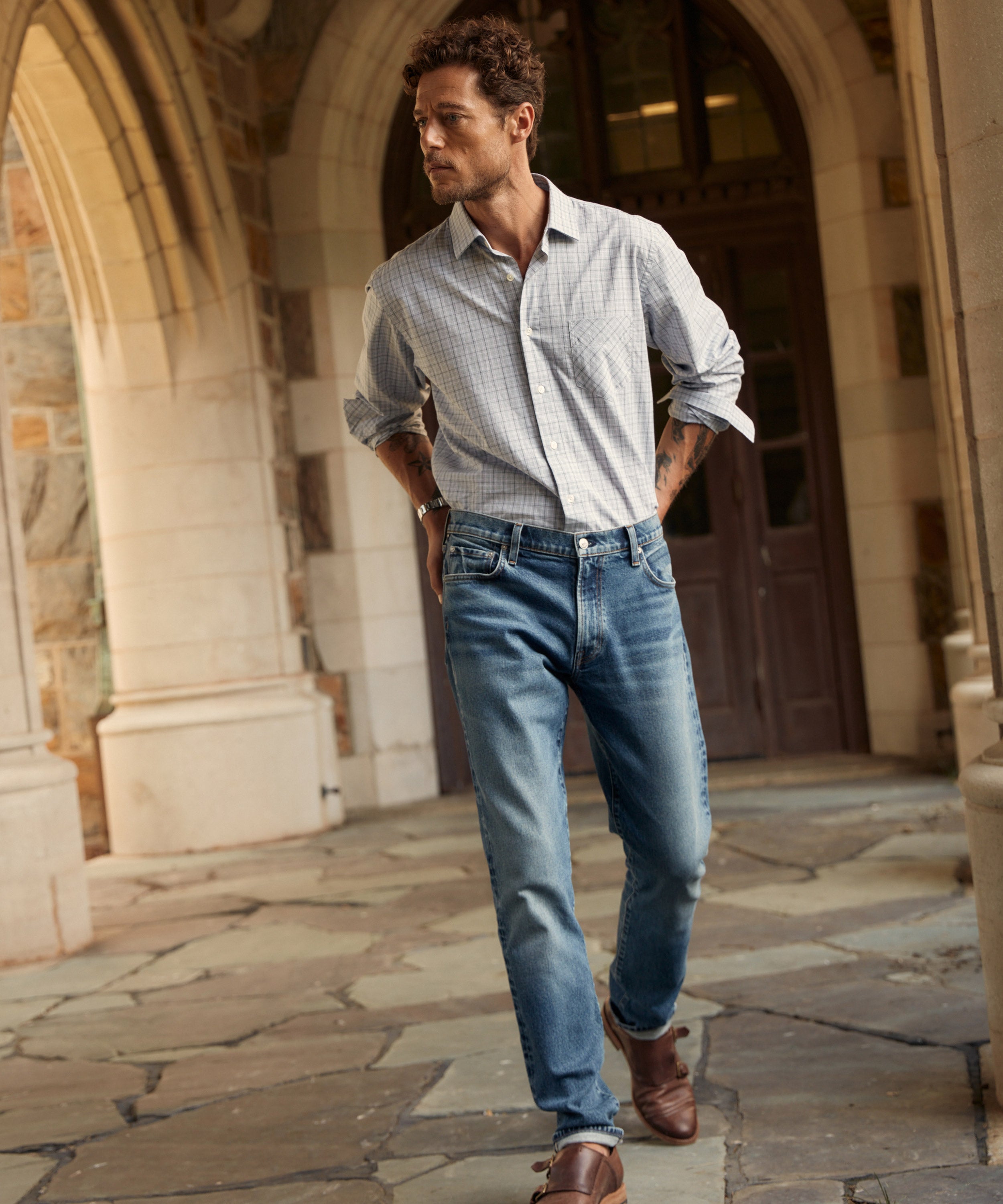 A male model wearing Billy Reid x Citizens jeans walks through a hallway, toward the camera.