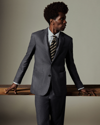 Man in a gray suit with a striped tie leaning against a wooden surface.