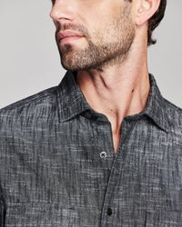 Close-up of a man wearing a dark gray textured button-down shirt, showing the collar, chest area, and part of his face against a light gray background.