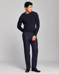 A man modeling a dark navy blue crewneck sweater and matching navy trousers with black dress shoes, standing against a light gray studio background.