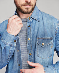 Model adjusts the collar of a denim shirt.