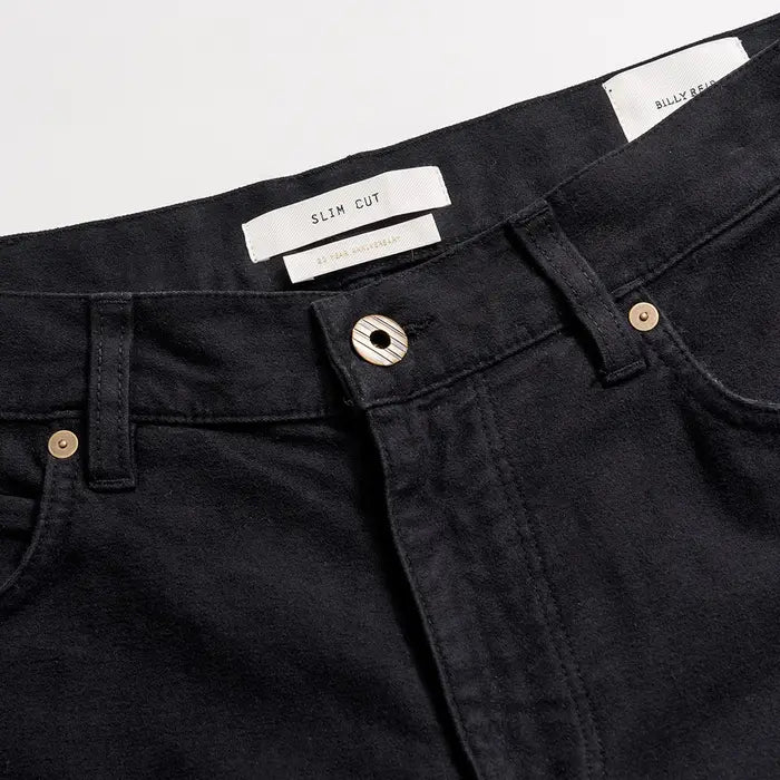 Close-up of black jeans with visible brand labels on a light gray background
