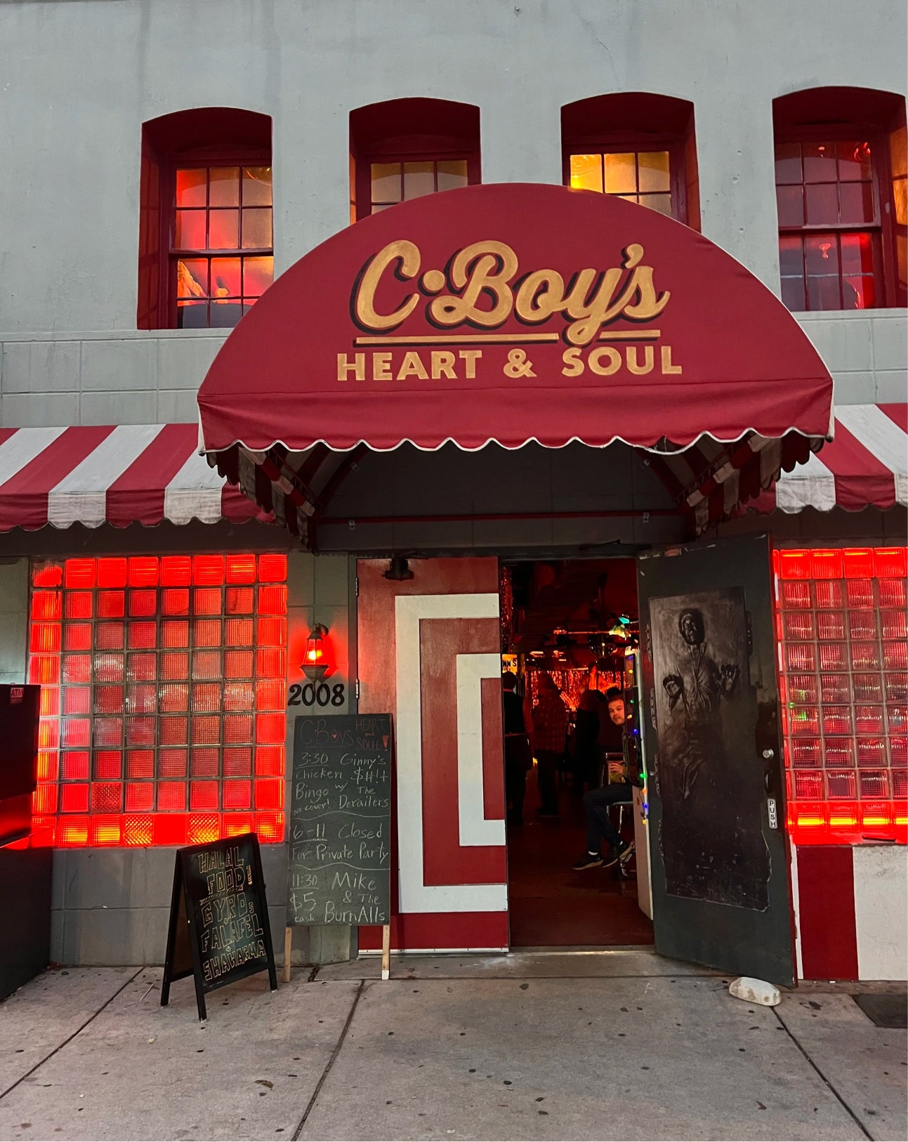 C-Boy's Heart & Soul restaurant storefront with a red awning, red-and-white striped awning, illuminated red glass block windows, and an open doorway showing the interior.