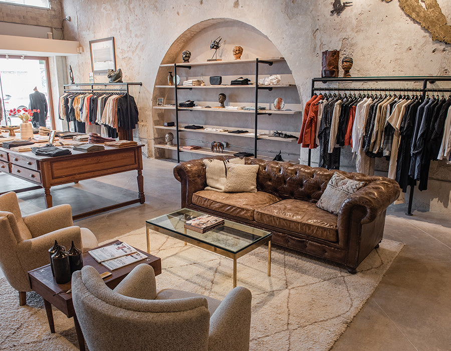 Luxury clothing store interior with leather sofa, armchairs, and clothing racks.