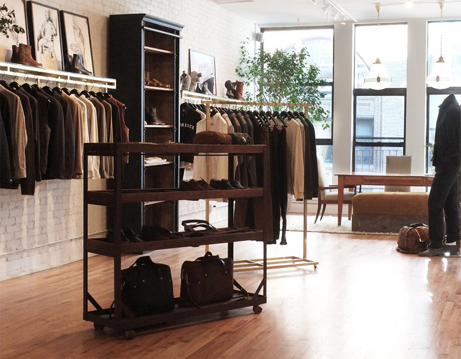 Clothing store interior with racks of clothes and bags on a wooden floor.