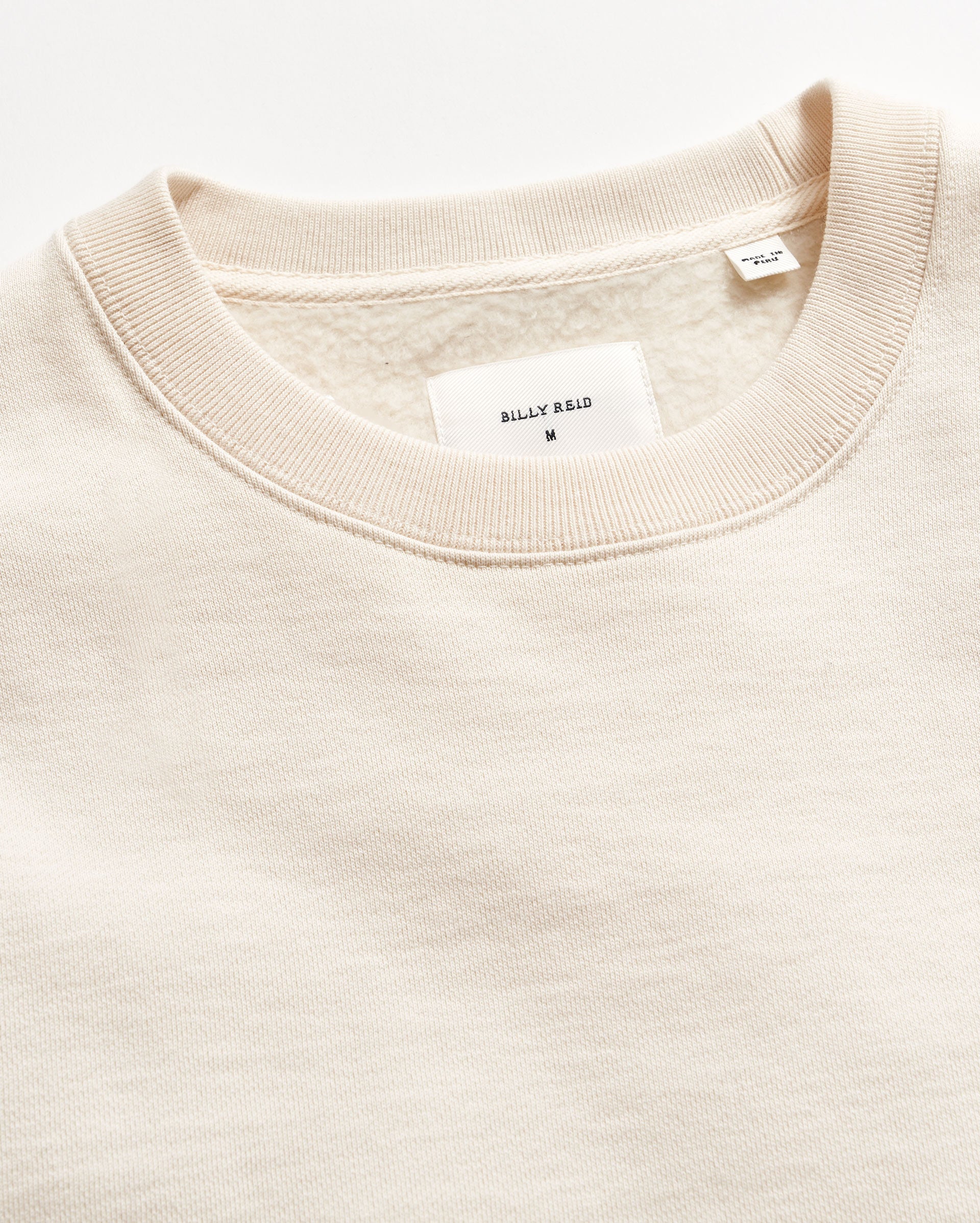 Close-up of a beige sweater with a brand label on a white background