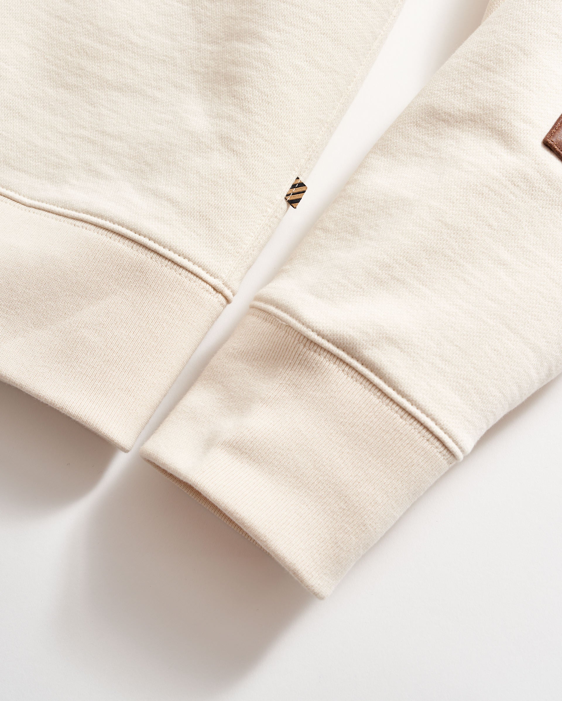 Close-up of a beige hoodie with a brand logo on a light background