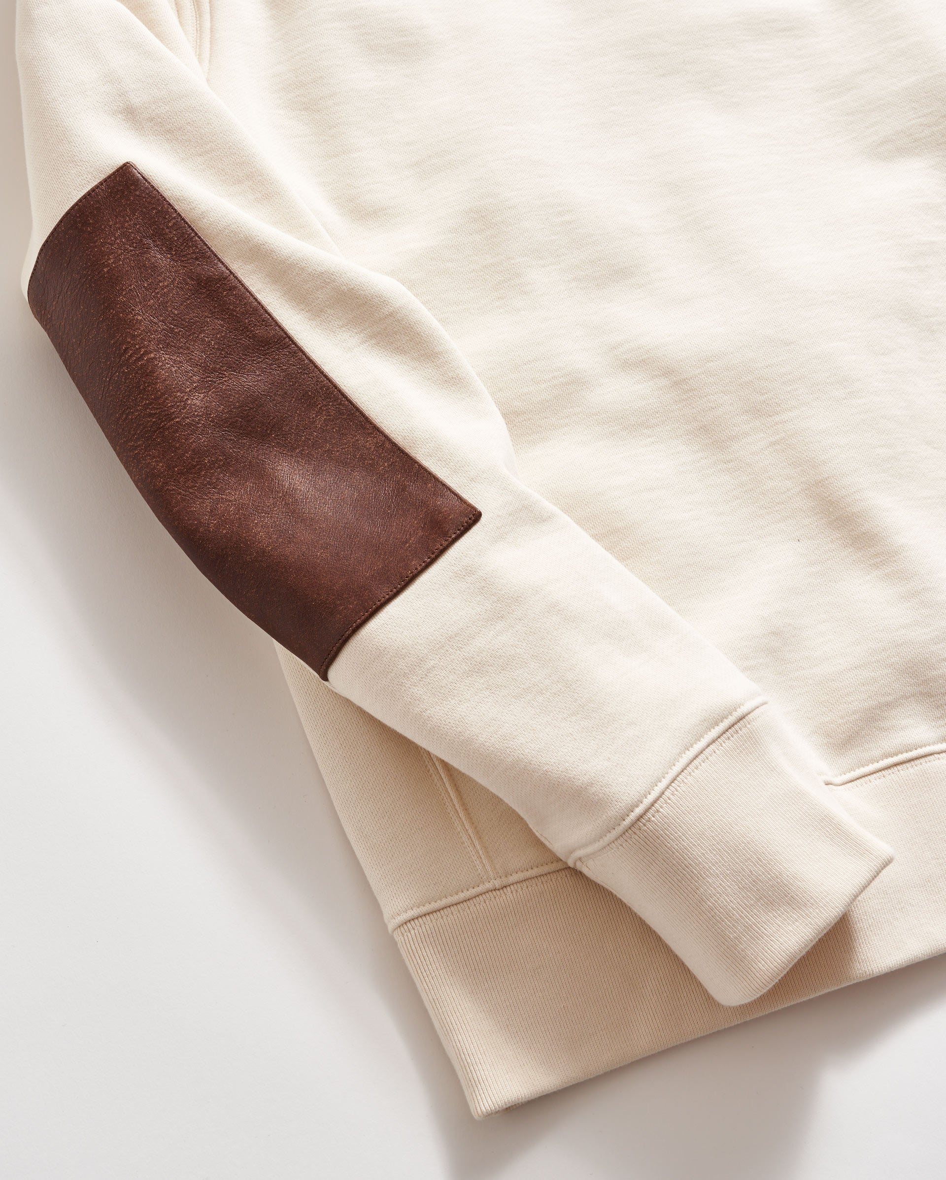 Close-up of a beige sweatshirt with brown arm patch on a light background