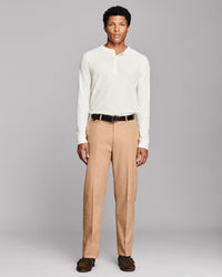 A man modeling a cream long-sleeve henley shirt and tan trousers with a black belt, standing against a solid gray studio background.