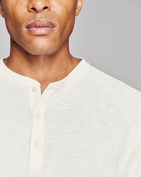 Close-up of a man wearing a textured off-white henley shirt against a plain gray background.