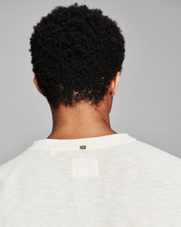 Back view of a person with curly black hair wearing a white textured crewneck sweater against a solid gray background.