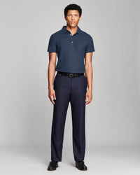 A man modeling a navy blue short-sleeve polo shirt and matching navy trousers with a black belt, standing against a light gray studio background.