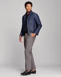 A man modeling a navy blue denim jacket over a black striped shirt, paired with grey flared trousers and black leather shoes, against a light gray studio background.