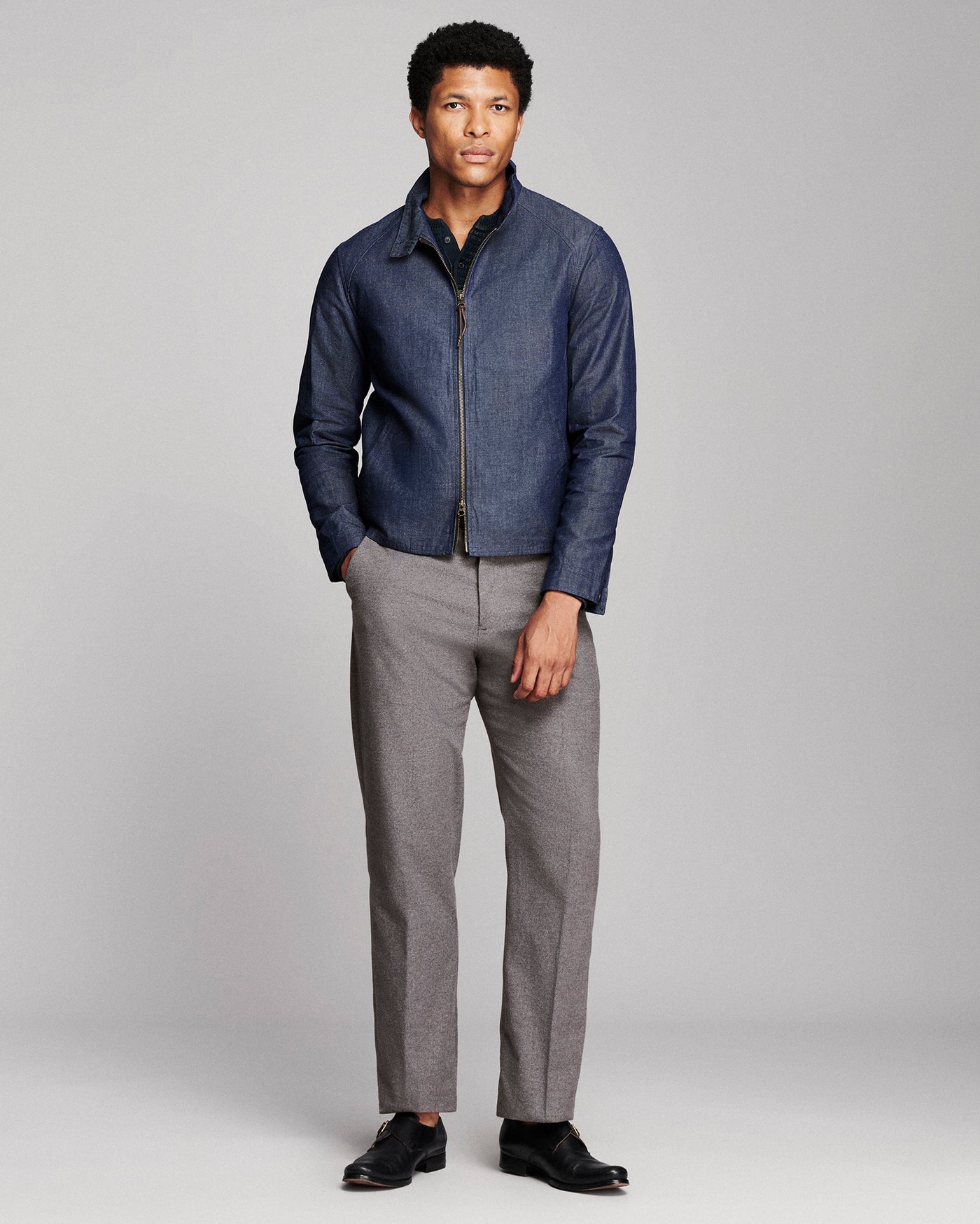 A man modeling a dark blue zip-up jacket and gray trousers against a light gray studio background.