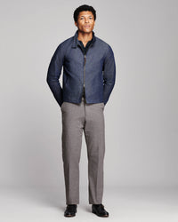 A man modeling a dark blue zip-up jacket with a dark collar, paired with gray trousers and black shoes, standing against a light gray studio background.
