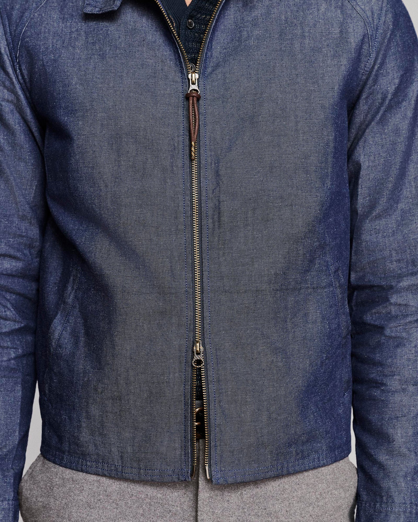 A close-up of a person wearing a blue denim zip-up jacket over a dark shirt and gray pants.