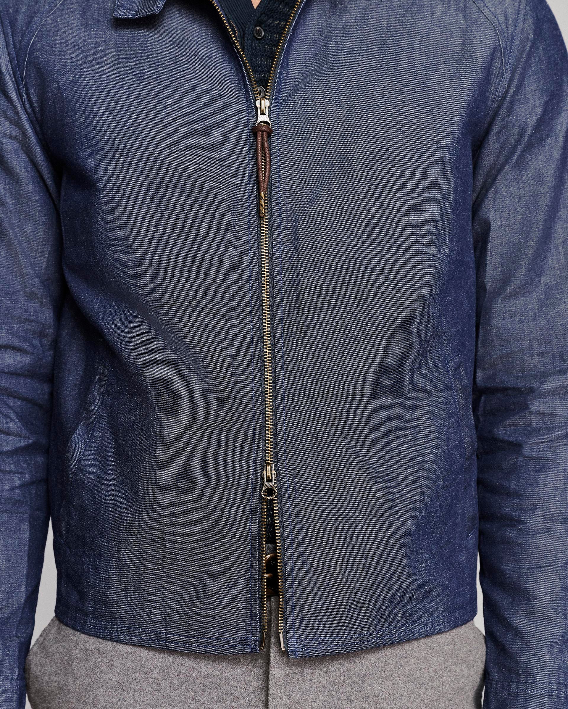 A close-up of a person wearing a blue denim zip-up jacket over a dark shirt and gray pants.