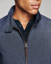 Close-up of a man wearing a blue textured zip-up jacket over a dark navy knit shirt, showing the collar, zipper, and fabric details against a neutral gray background.