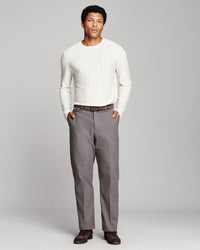 A man modeling a white ribbed long-sleeve knit sweater and gray trousers against a light gray studio background.