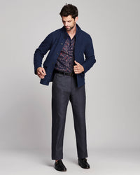 A man modeling a navy blue knit cardigan over a patterned shirt, paired with dark charcoal trousers and black loafers, against a light gray studio background.