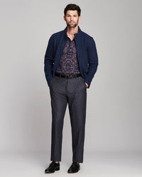A man modeling a dark navy blue knit cardigan over a patterned button-down shirt, paired with dark gray trousers and black dress shoes, against a light gray studio background.