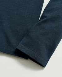 A close-up of a dark blue long-sleeve shirt sleeve laying flat on a light surface, showing the fabric texture and stitching detail at the cuff and hem.