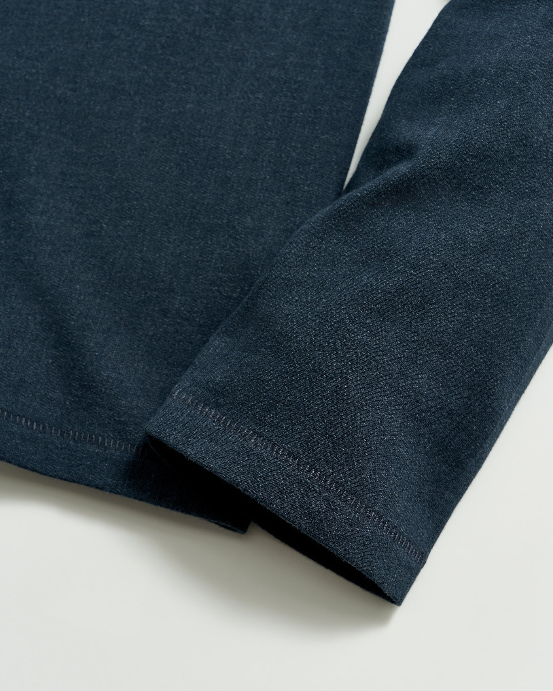 A close-up of a dark blue long-sleeve shirt sleeve laying flat on a light surface, showing the fabric texture and stitching detail at the cuff and hem.