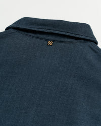 Close-up of the back of a dark blue collared shirt, showing a small, striped loop detail just below the collar on a plain white background.