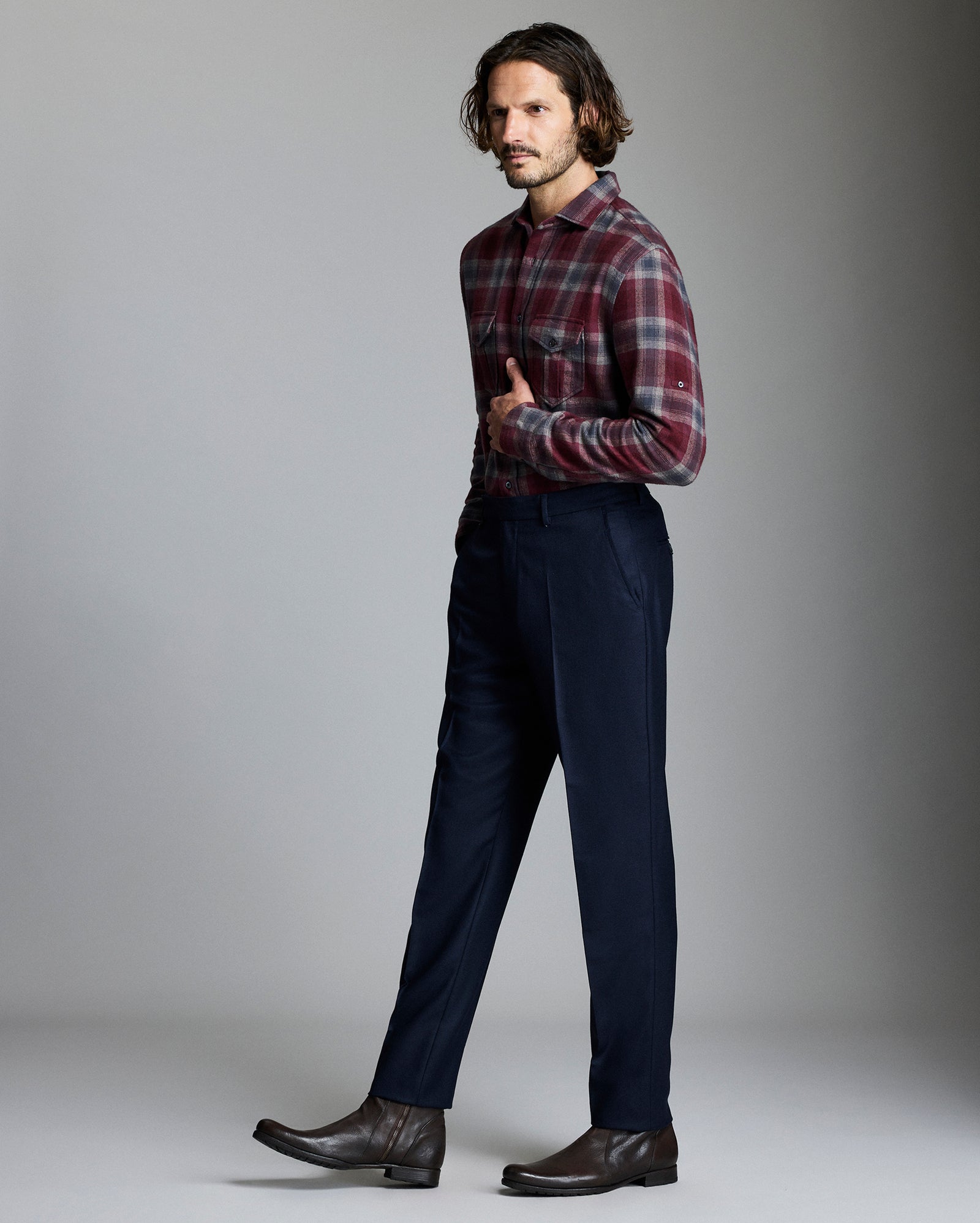 Man wearing a plaid shirt and dark pants against a gray background