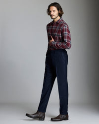 Man wearing a plaid shirt and dark pants against a gray background