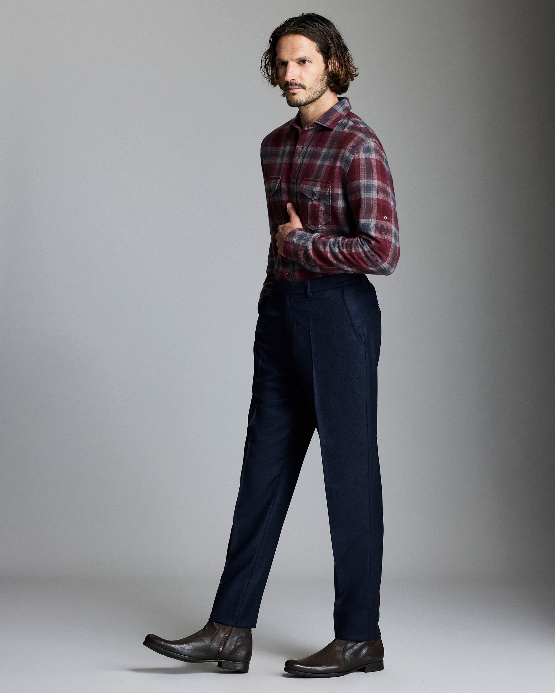 Man wearing a plaid shirt and dark pants against a gray background