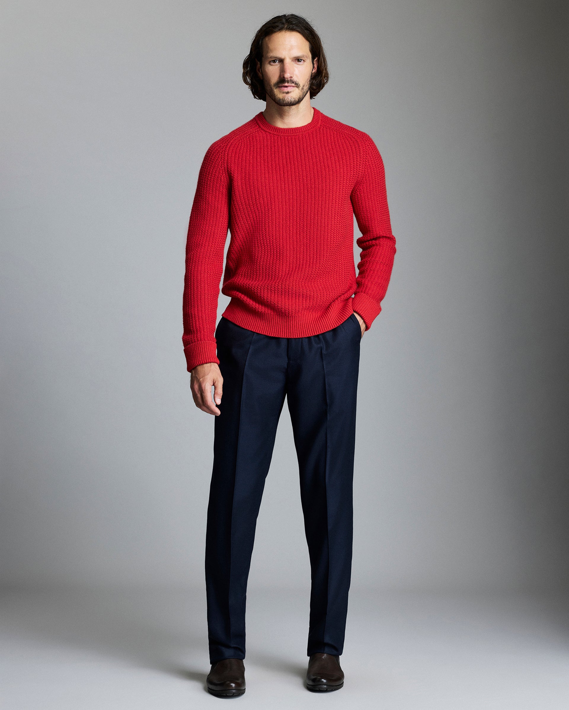 Man wearing a red sweater and navy pants against a gray background