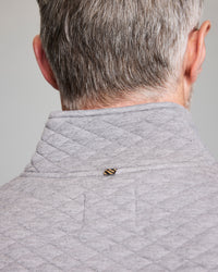 A person with short gray hair is seen from behind, wearing a light gray, quilted jacket. A small black and yellow bee is perched on the collar.