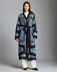 Woman wearing a long, patterned coat against a plain background