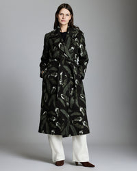 Woman wearing a black patterned coat with white pants on a gray background