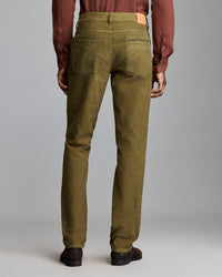 A person stands facing away, wearing olive green pants, a brown long-sleeve shirt, and dark brown shoes against a plain gray background.