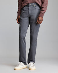A person wearing a maroon sweater, gray pants, and white sneakers stands against a plain gray background. Only the lower half of their body is visible.