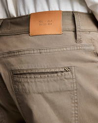 Close-up of the back waistband and pocket of khaki pants. A tan leather patch with the text MSL • ALA RN-113 814 is sewn above the pocket. A white shirt is partially visible above the pants.