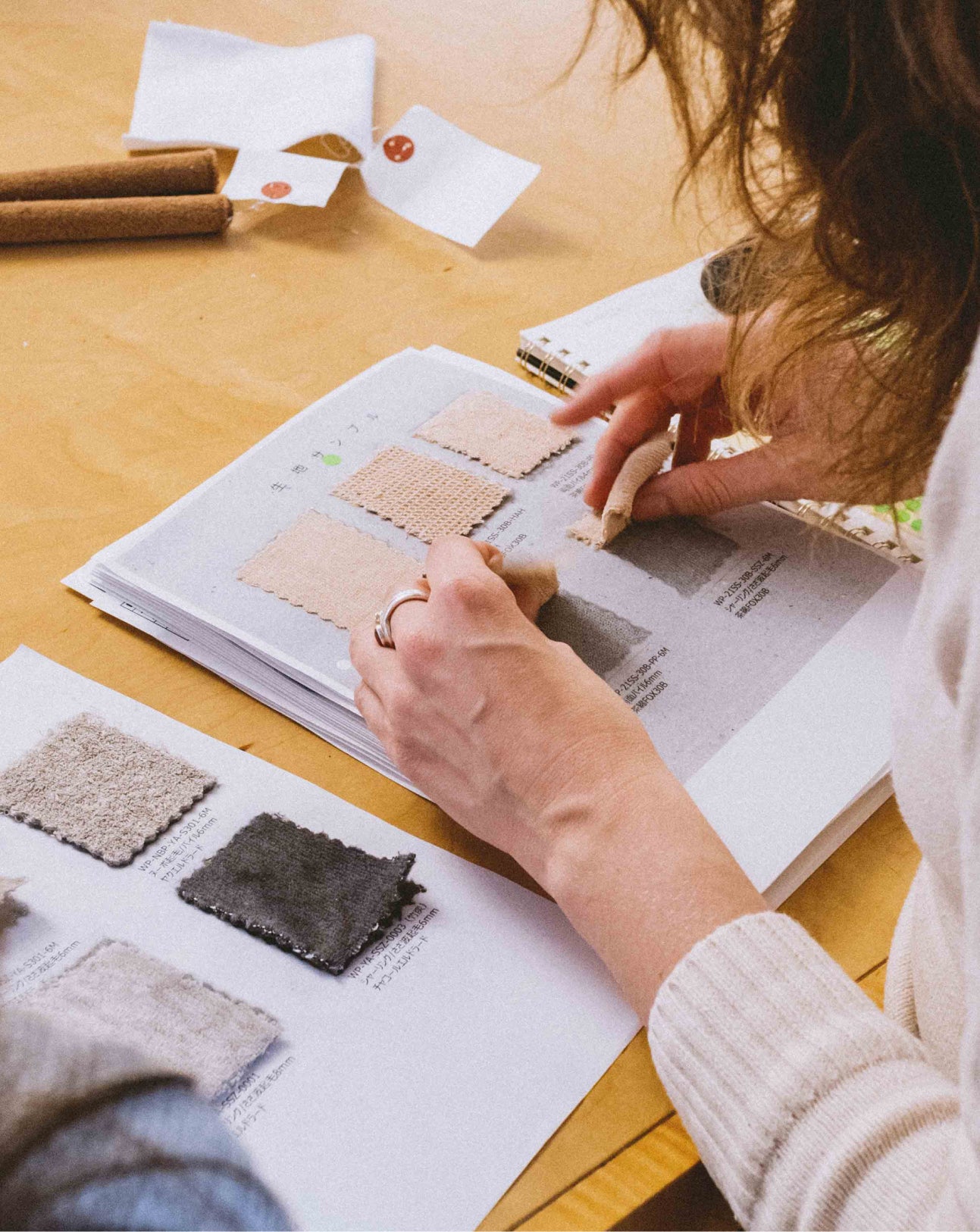 Person comparing fabric swatches in a book on a wooden table