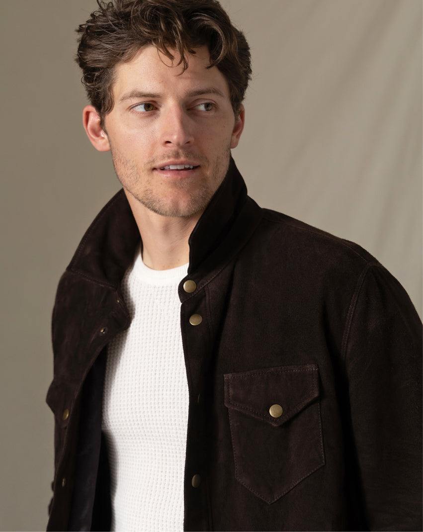 Man wearing a dark brown jacket over a white shirt against a plain background