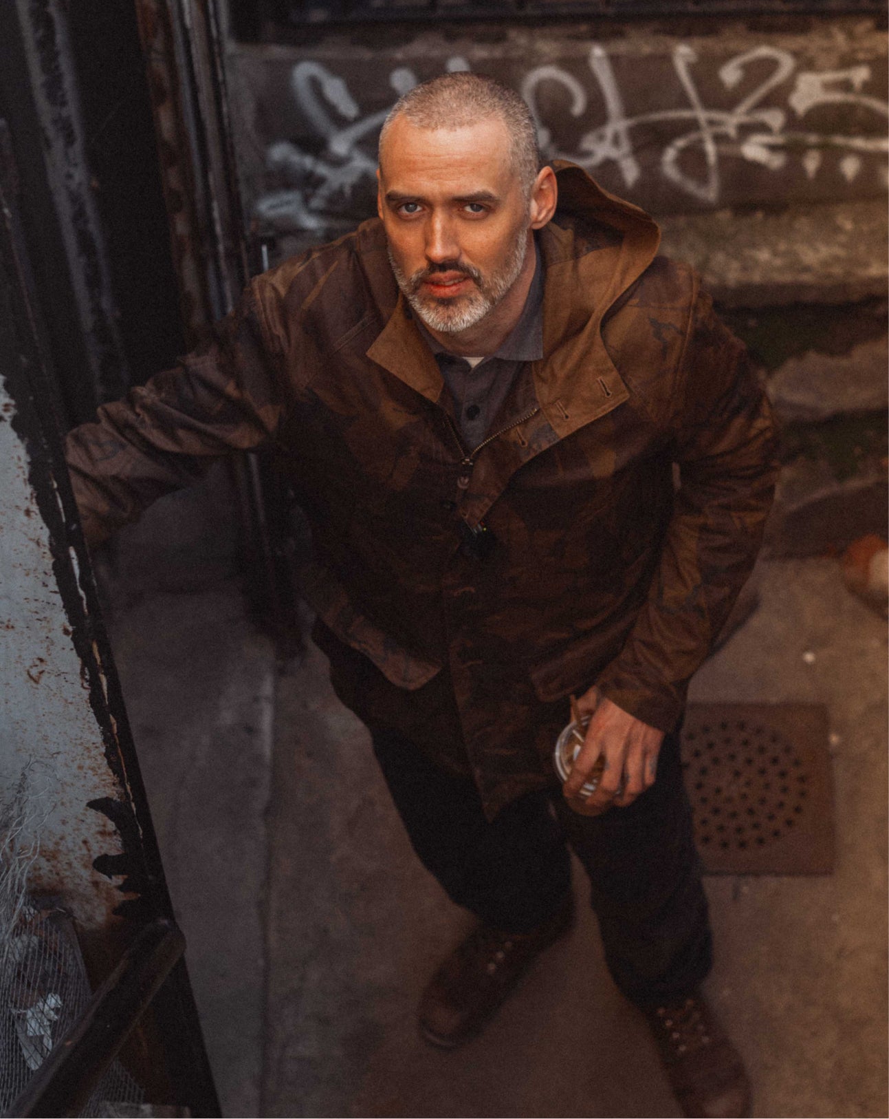 Man in a brown coat leaning against a wall with graffiti