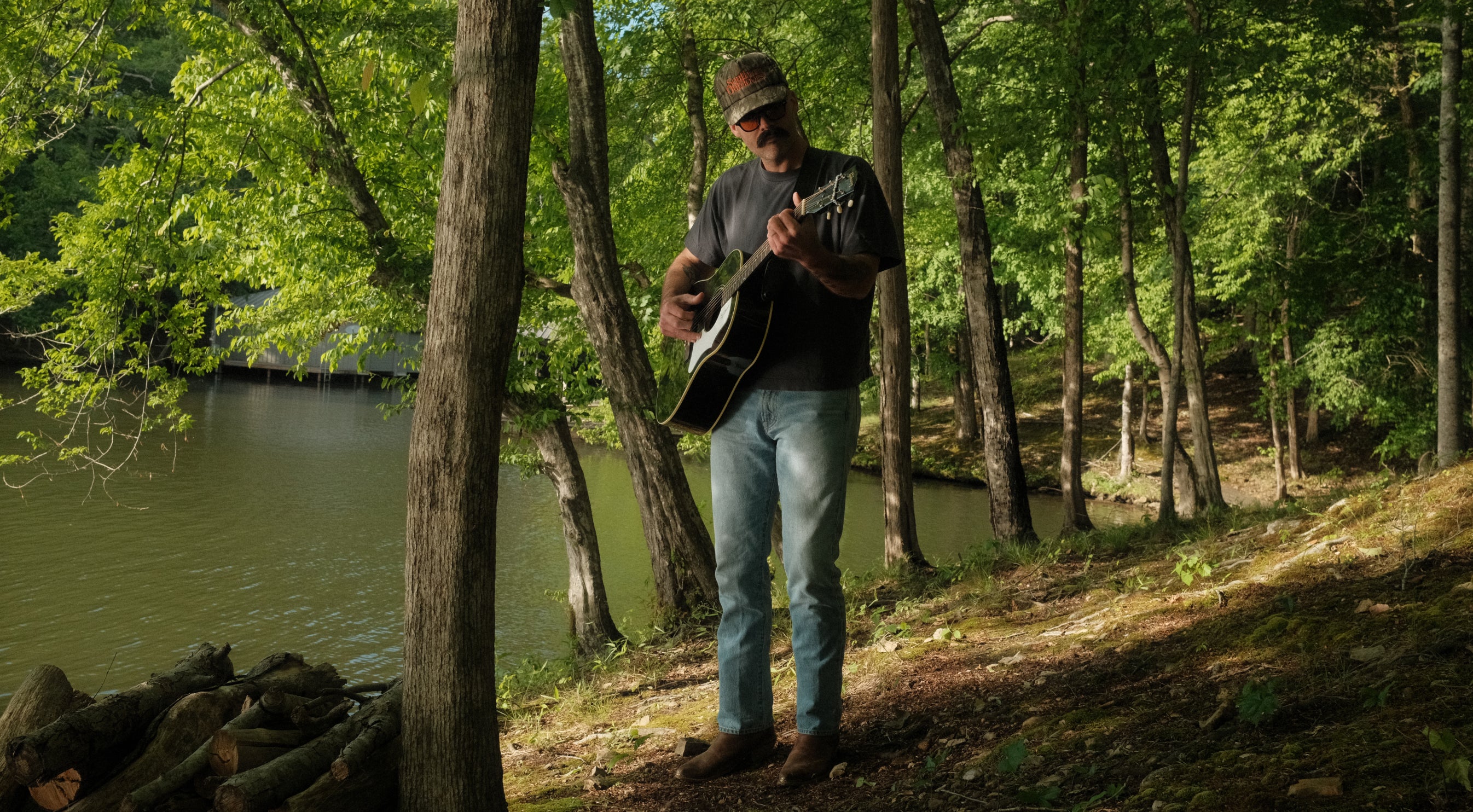 Man playing guitar in a forest by a lake