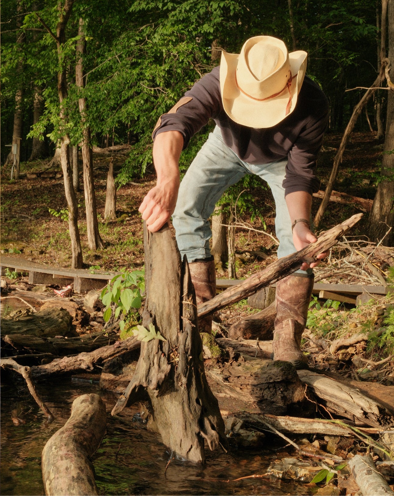 Man in cowboy hat and boots standing on a log in a forest setting