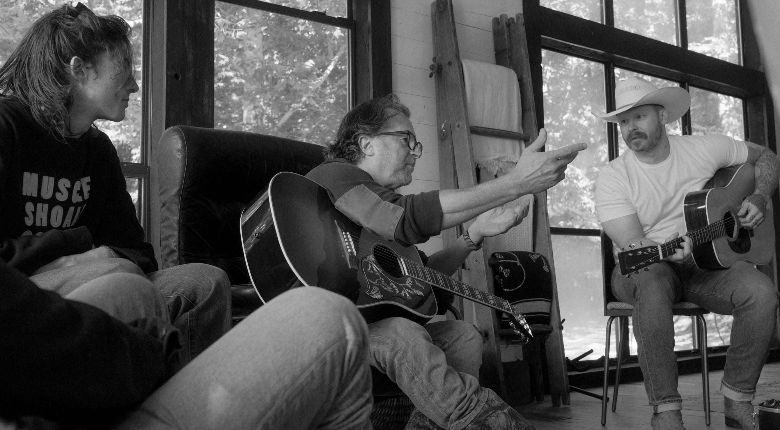 Three people playing guitars in a room with large windows