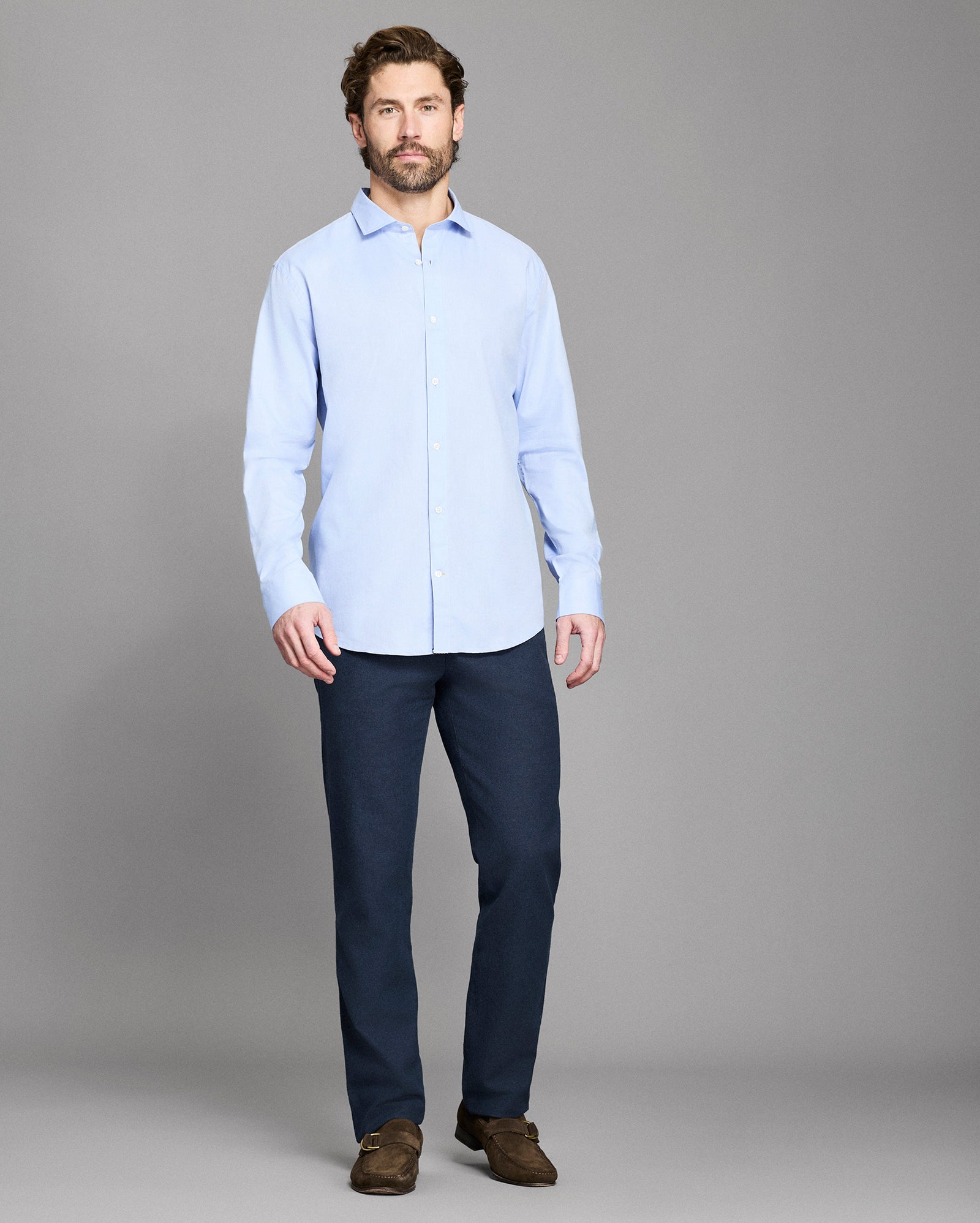 Man wearing a light blue shirt and dark pants against a gray background