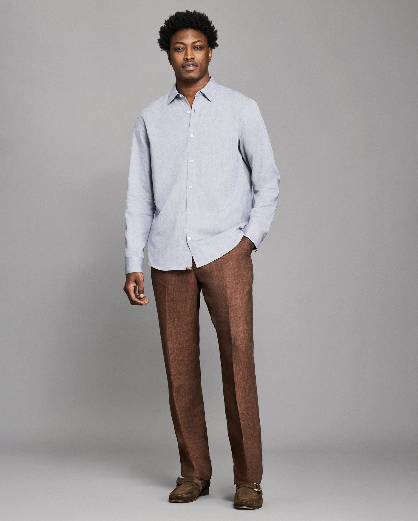 Man wearing a light gray shirt and brown pants against a plain background
