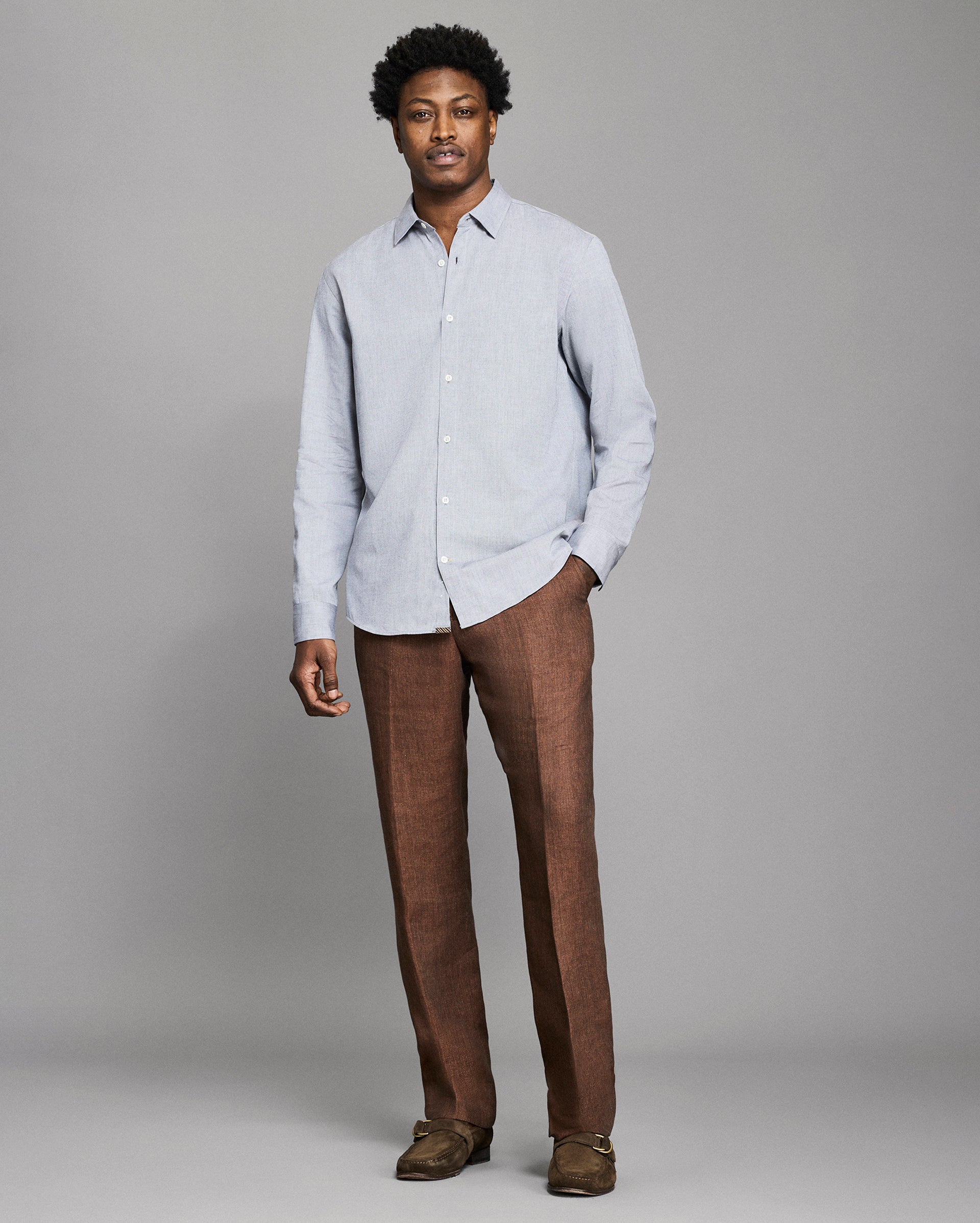 Man wearing a light gray shirt and brown pants against a plain background