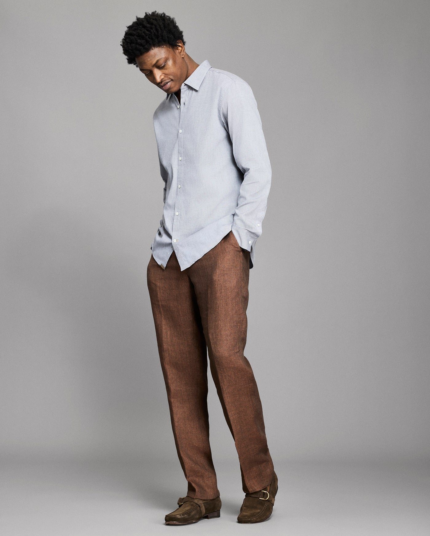 Man wearing a light blue shirt and brown pants against a gray background