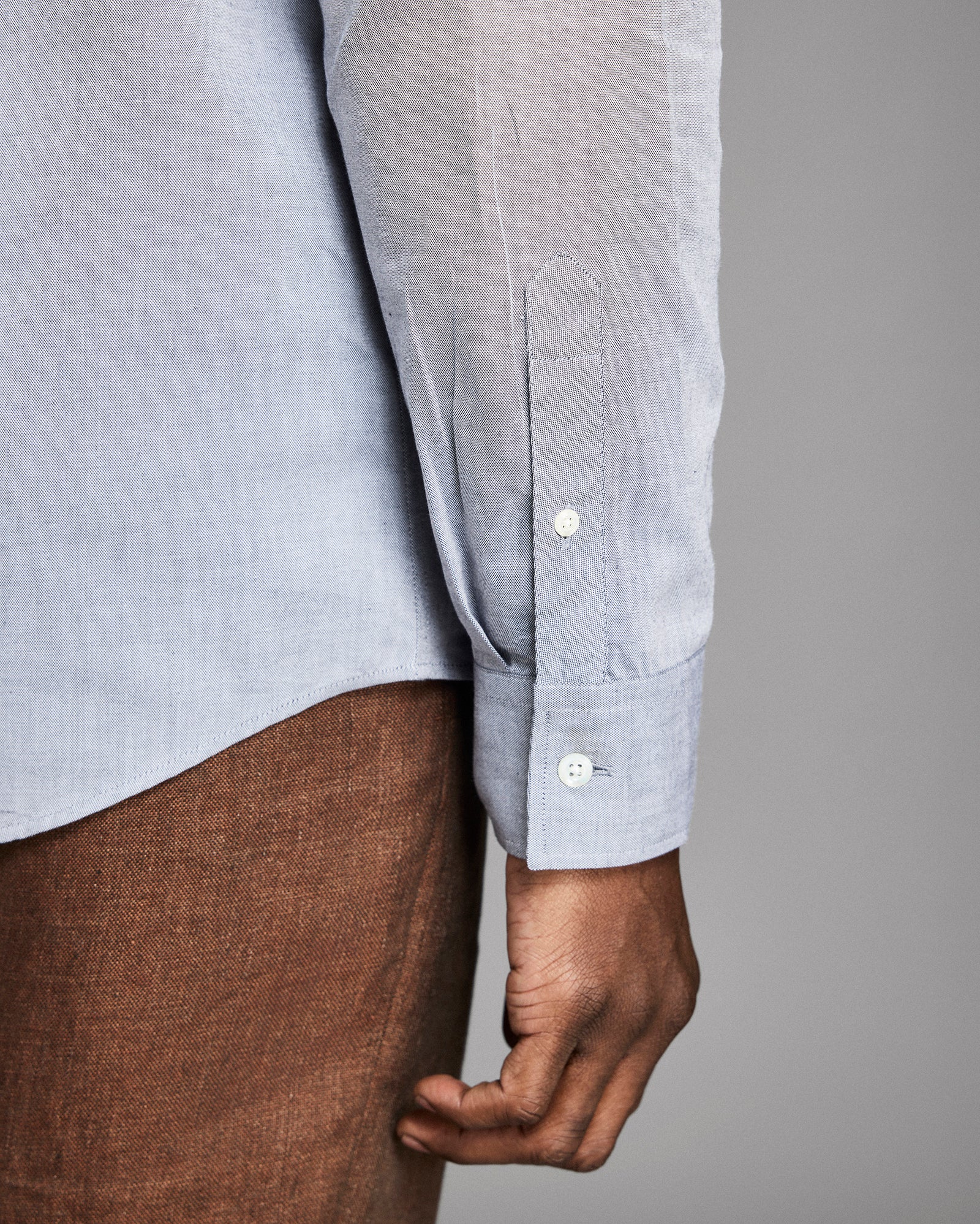 Close-up of a person wearing a light blue shirt with rolled-up sleeves against a gray background