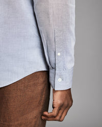 Close-up of a person wearing a light blue shirt with rolled-up sleeves against a gray background